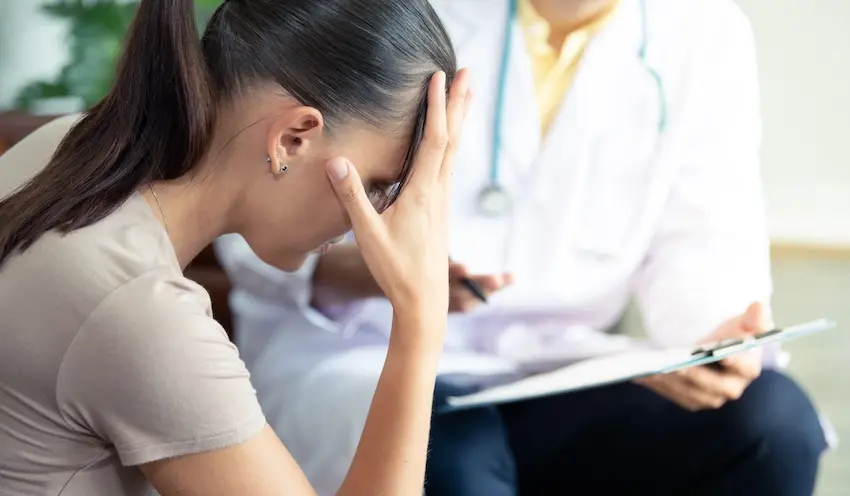 A distressed woman is holding head in pain during a medical consultation discussing traumatic brain injuries and treatment options in North Carolina.