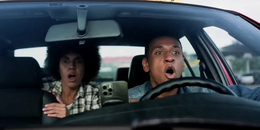 A male driver and female passenger both react with wide-eyed shock and open mouths while inside an Uber capturing the terrifying split-second moment of impact that victims experience in rideshare accidents in North Carolina.