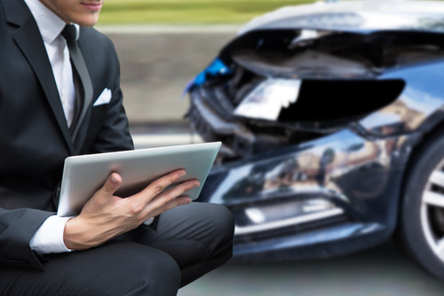 Adjuster inspects a damaged car representing insurance company tactics after a car accident