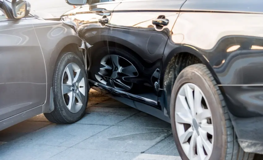 Two dark-colored vehicles are pressed tightly together with crushed and crumpled door panels visible between them showing the type of side-impact collision damage commonly seen in rideshare accidents on busy city streets and could use assistance from NC Injury Law.